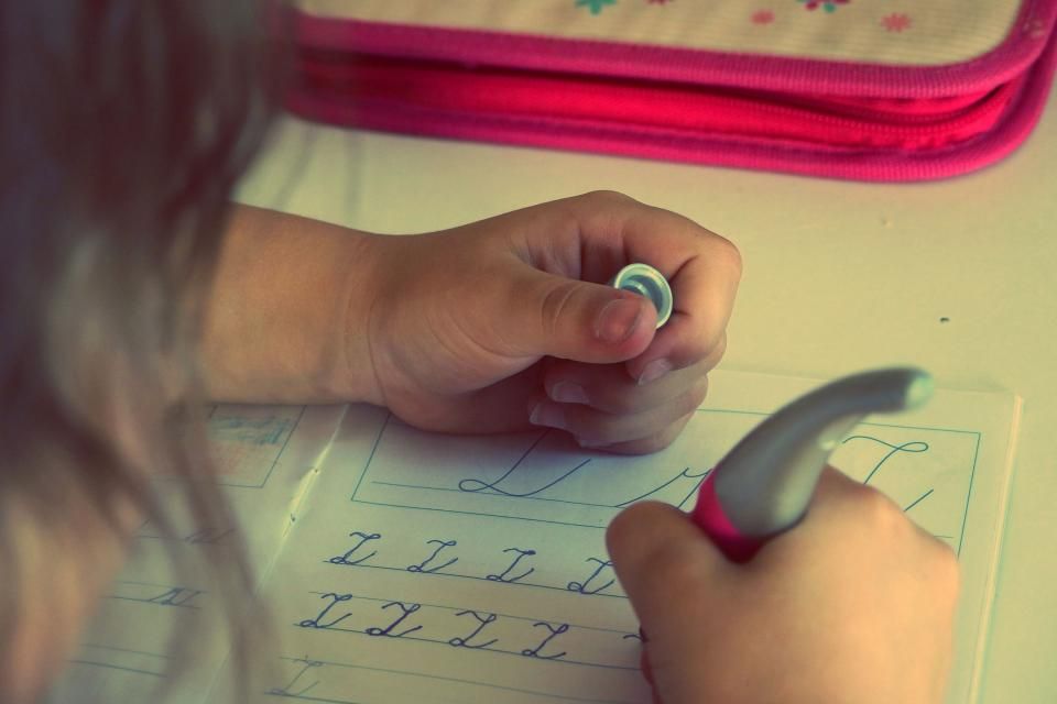 Mano de una niña o niño escribiendo en un cuaderno con un lápiz de color
