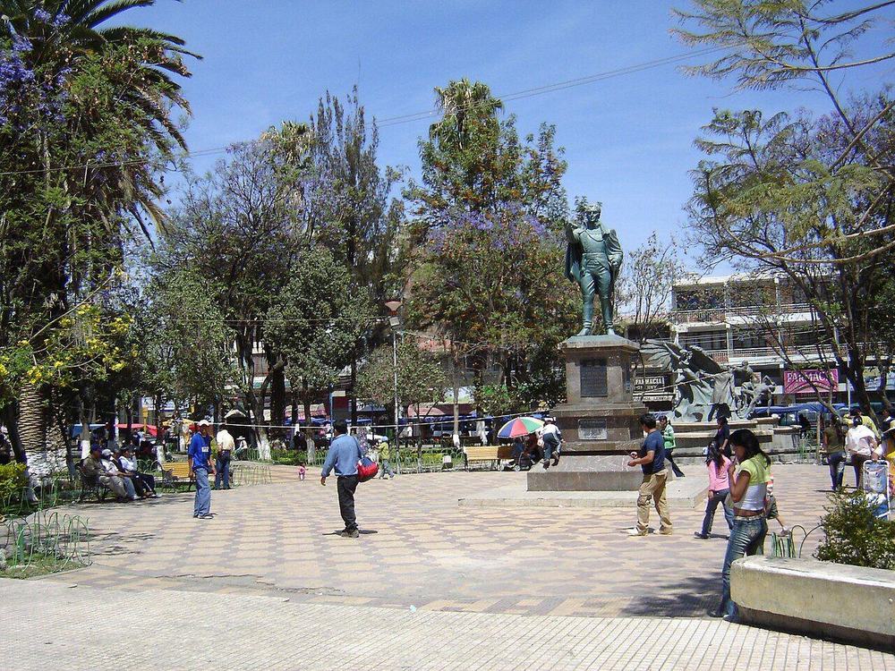 Plaza Bolívar de Quillacollo, con palmeras, bancos y la iglesia al fondo